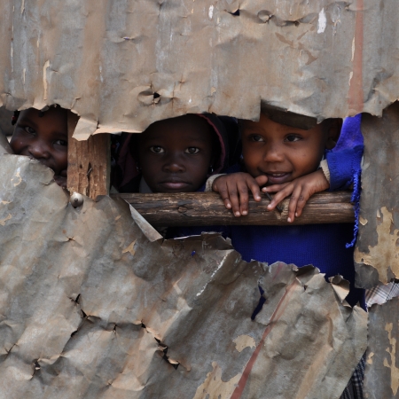Kenyan children peek through a broken tin wall