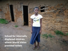 Girl standing in front of a mud and wattle school, DR Congo